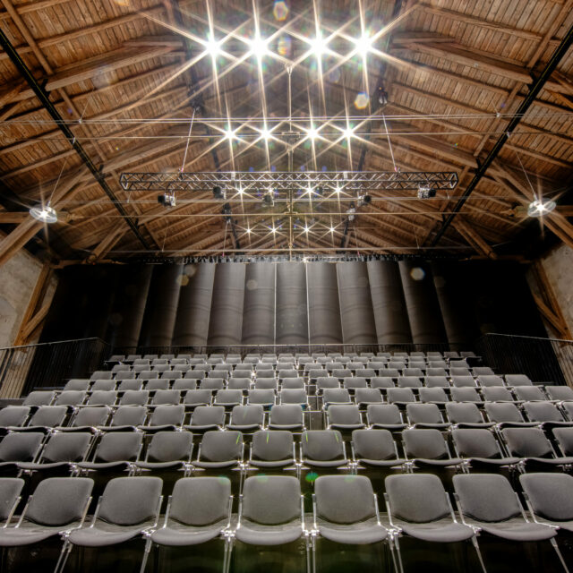 Acoustically effective roller banners behind the rows of seats of a former riding hall